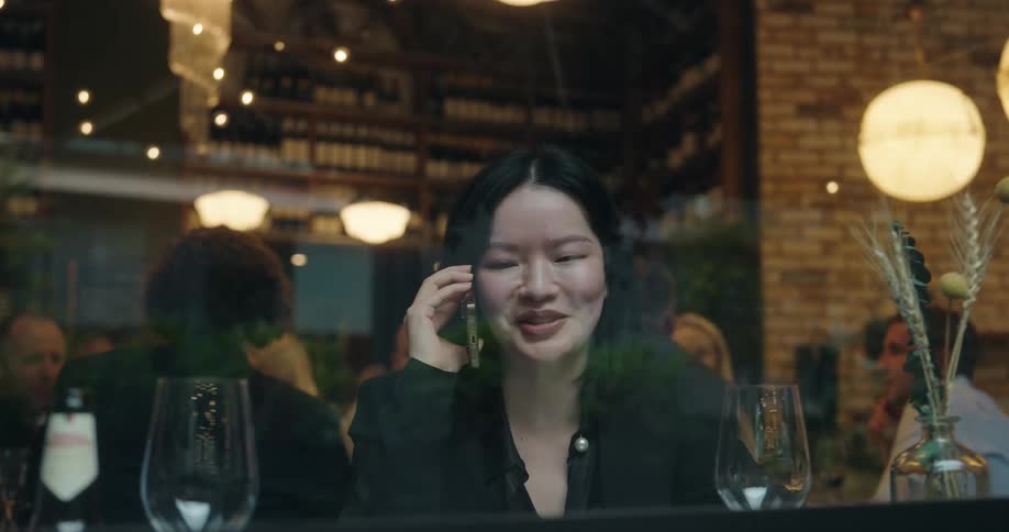 A woman in a restaurant is sitting at a table talking on her phone