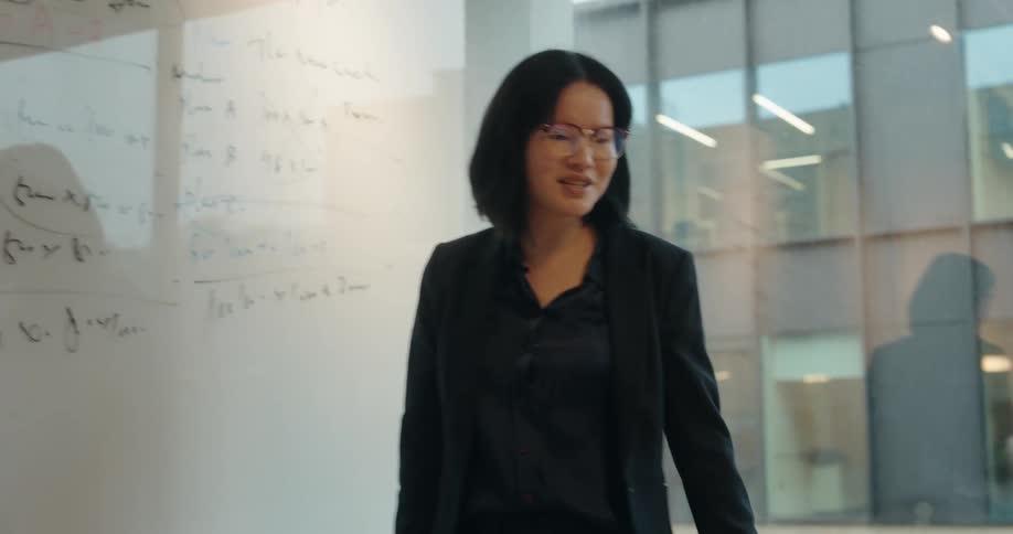 Woman references the writing on a whiteboard while giving a presentation