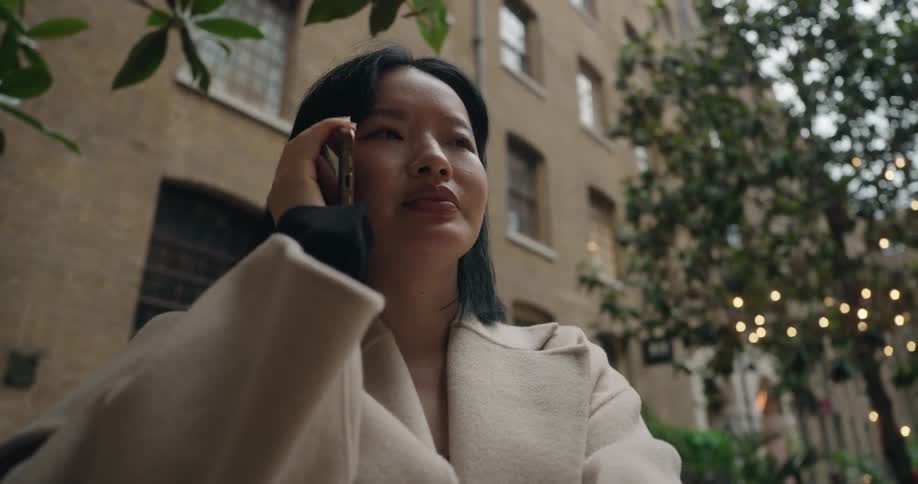 Woman standing outside in front of an apartment building as she talks on her phone