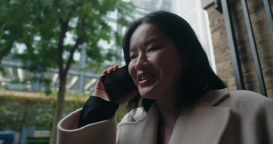 Young asian woman wearing a heavy coat standing on the streets talking on a smartphone on a metropolitan area during day time
