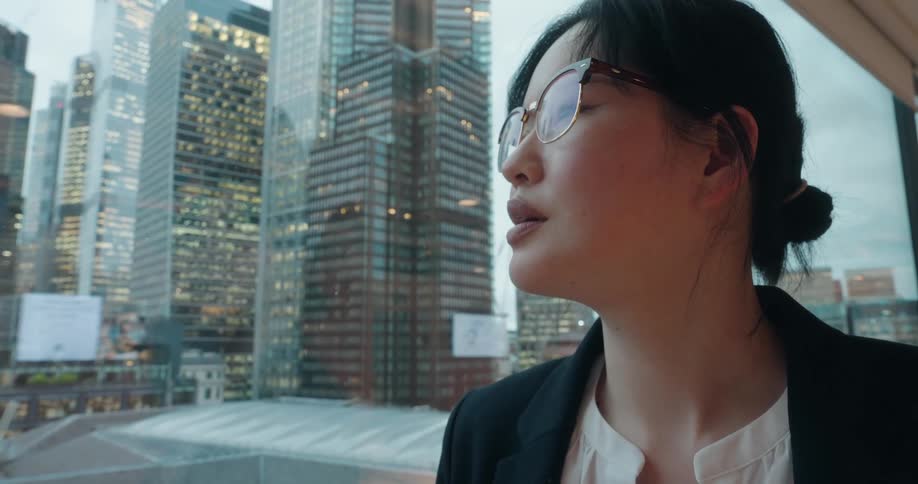 Woman wearing glasses looks at something offframe with illuminated buildings in the background