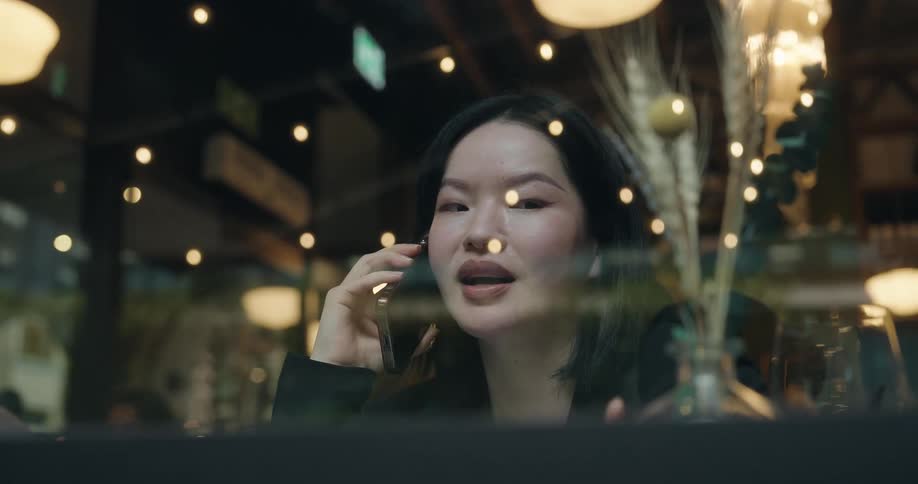 A woman is sitting behind glass as she talks on her cellphone