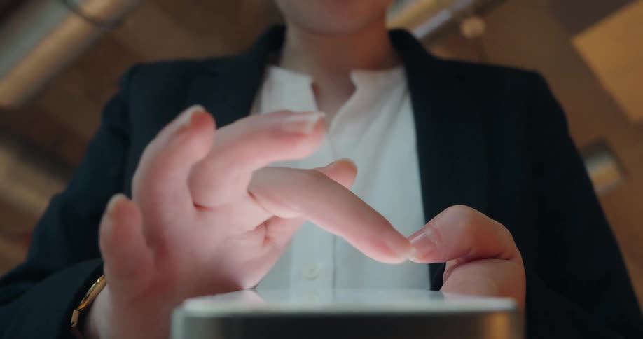 A close view of a woman in a black blazer and white shirt using her fingers to interact with the bright screen of a smartphone