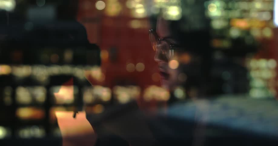 Reflection of a lit city and a person reading near a window