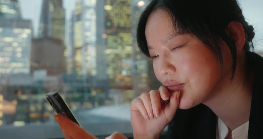 Woman looks at her phone with illuminated buildings in the background at dusk