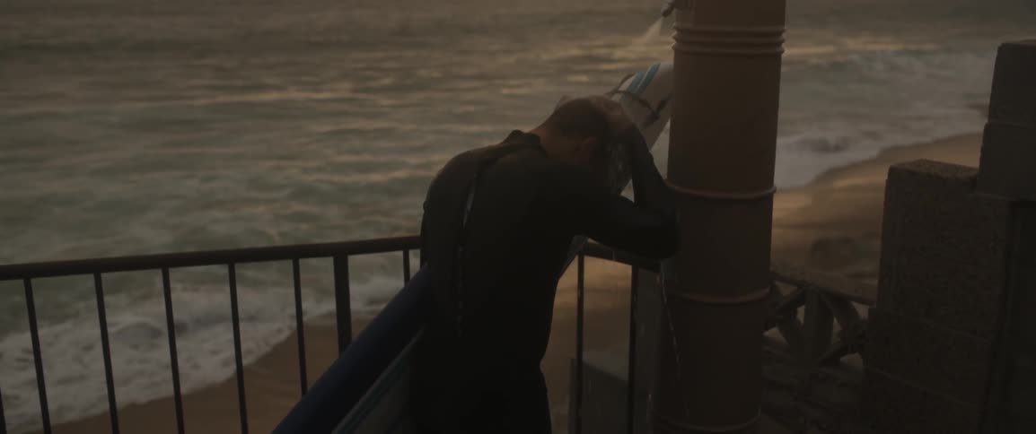 A man whips his hair back holding a surfboard