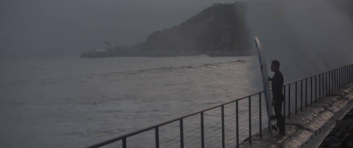A man is holding a surfboard by the water