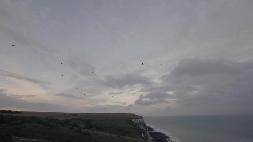 Birds fly high in the sky by this cliff