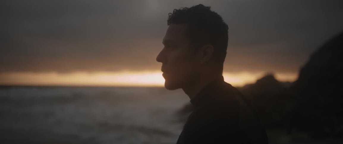 A man looks over the coast carrying a surfboard