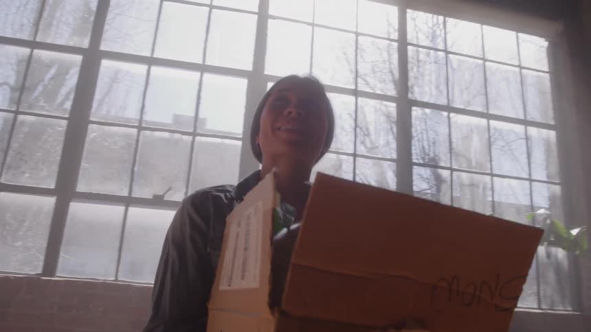 The woman is smiling and turning while holding a cardboard box