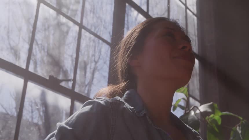 Woman smiling softly while looking at something near the sunlit windows