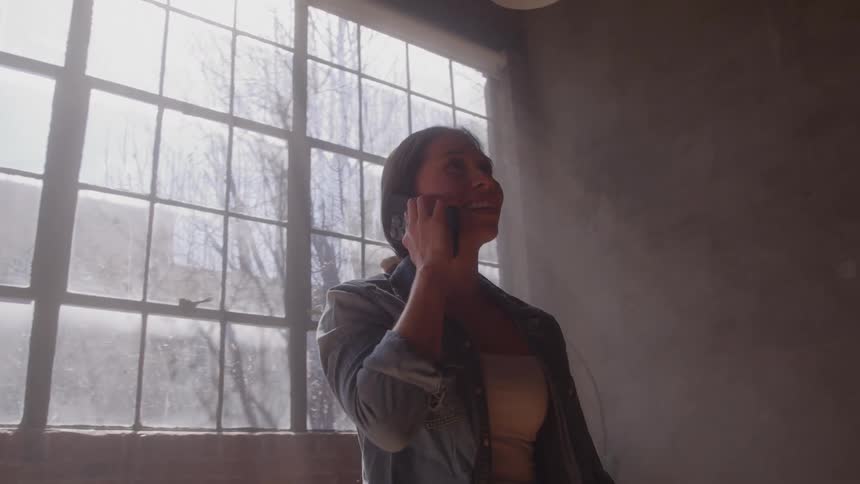 Woman smiles as she stands near windows talking on her phone