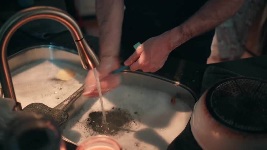 Hands wash dishes in a foamfilled sink under running water