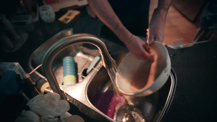 The man scrubs dishes in the sink