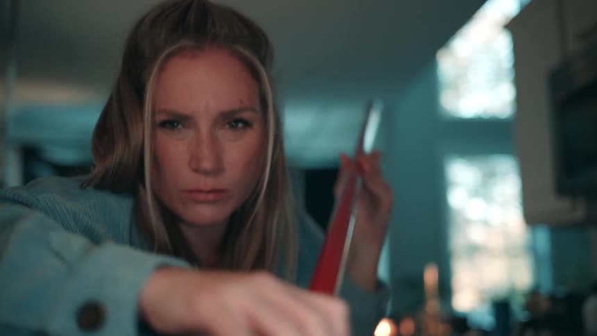 A woman with an intense expression as she vigorously sweeps a floor with a red broom and dustpan in a brightly lit kitchen