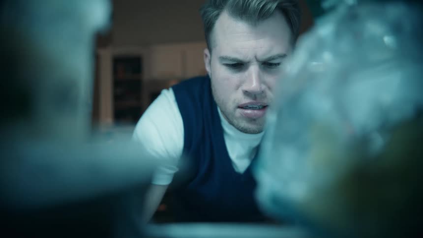 A man in a dark vest open the door bend down with a concerned expression to look inside search briefly take out a blue object and then stand back up as a woman appears in the background