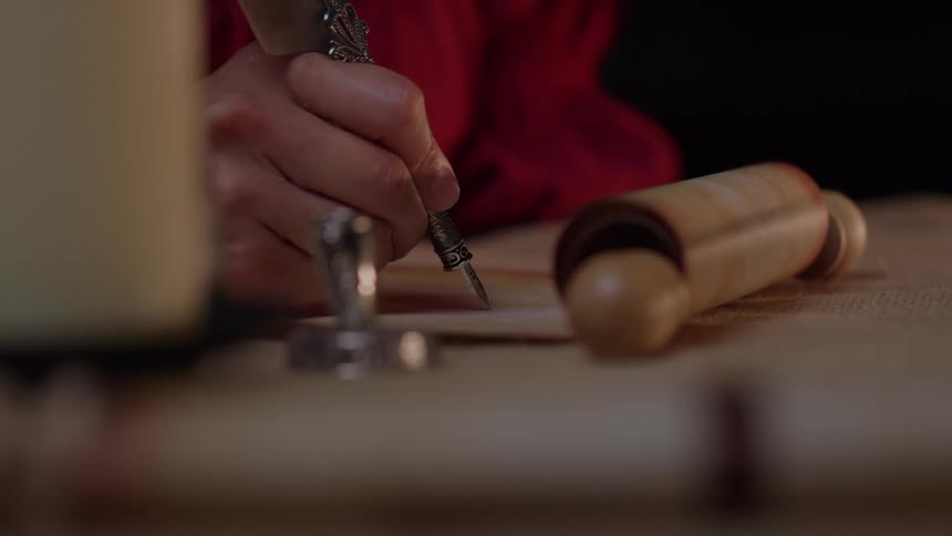 Hand writes with a quill beside a rolled parchment on the table