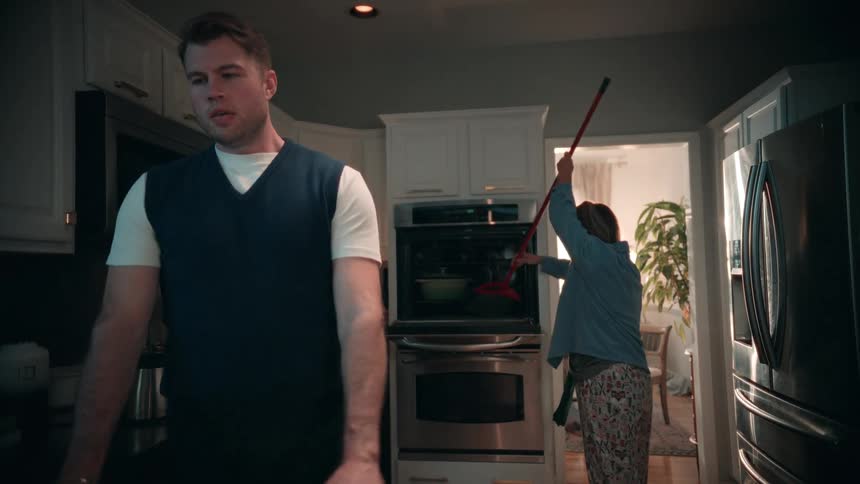 The man gets upset when he sees the woman sweeping the oven with a broom