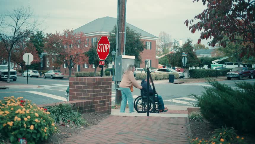 A woman is walking down the street pushing a man in a wheelchair