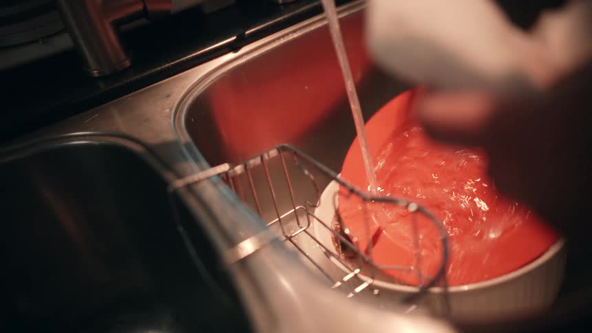 Hands of a person washing dishes under running water indoors
