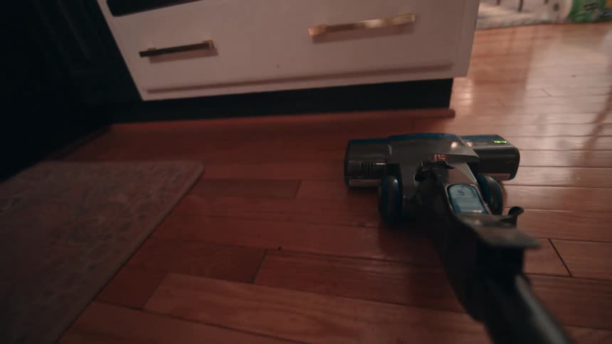A cordless vacuum cleaner moves across a polished hardwood floor in a room capturing a moment of domestic cleaning