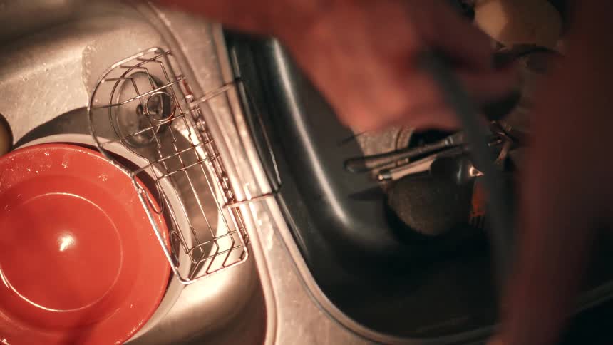 The man is washing dishes and spraying a hose