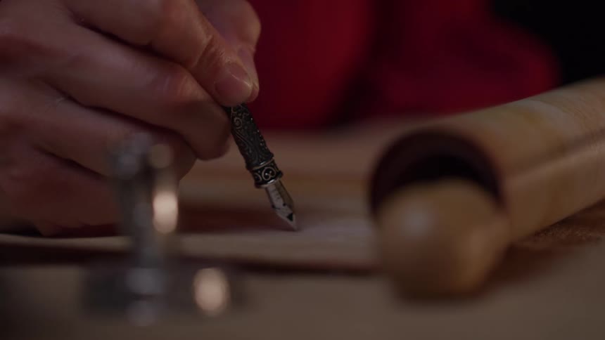 Hand holds a decorated metal nib while writing on parchment