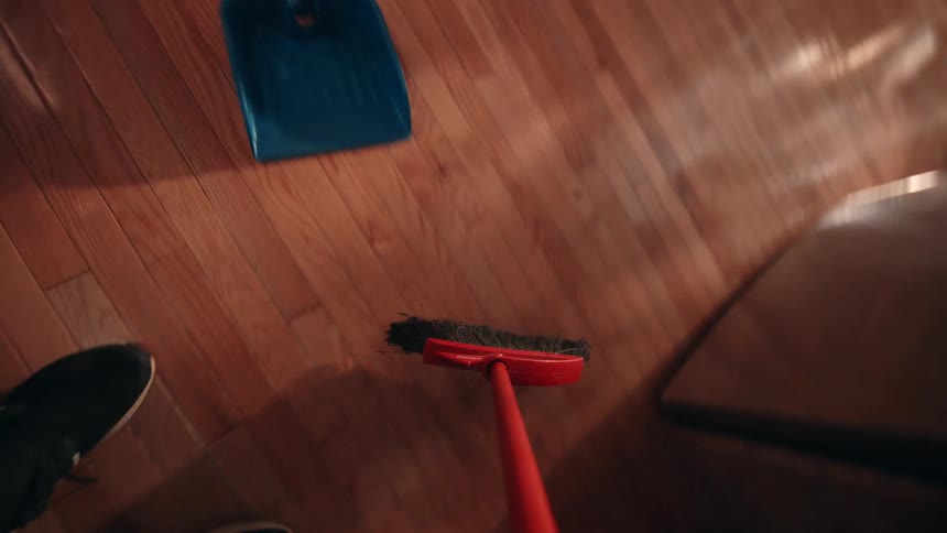 Red broomstick sweeping the floor and running into a shovel with a person standing next to it indoors during day time