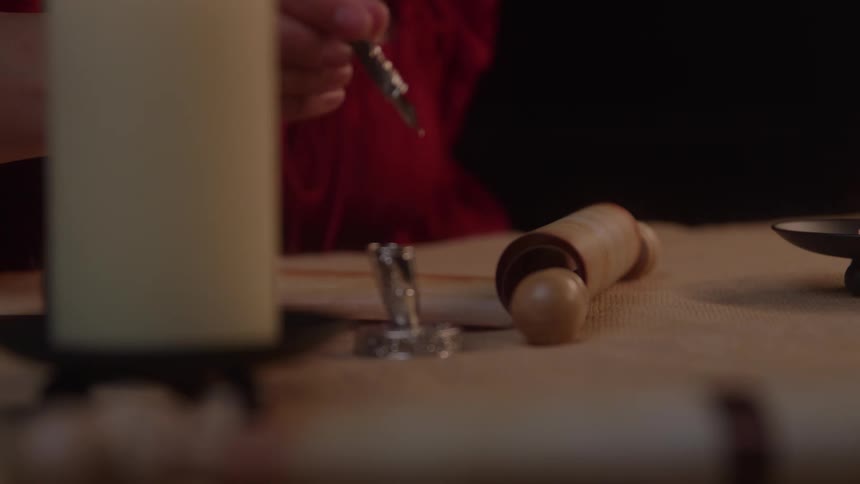 Hand writes with a quill beside a rolled parchment on the table