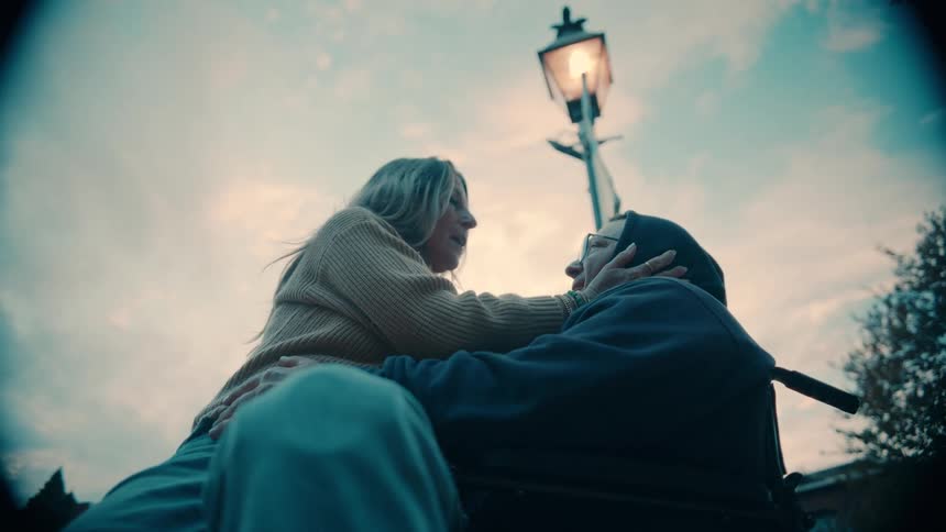 Woman leans in to talk with a man in a wheelchair at dusk