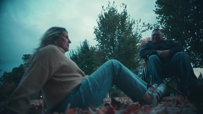 The woman sitting on leaves picks up a handful and tosses it