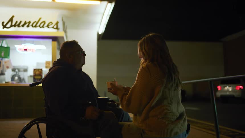 A woman eating ice cream stops to clean off a mans mouth with a napkin