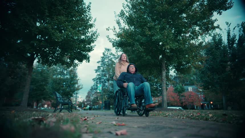 Couple moving through a park while the man rides in a wheelchair