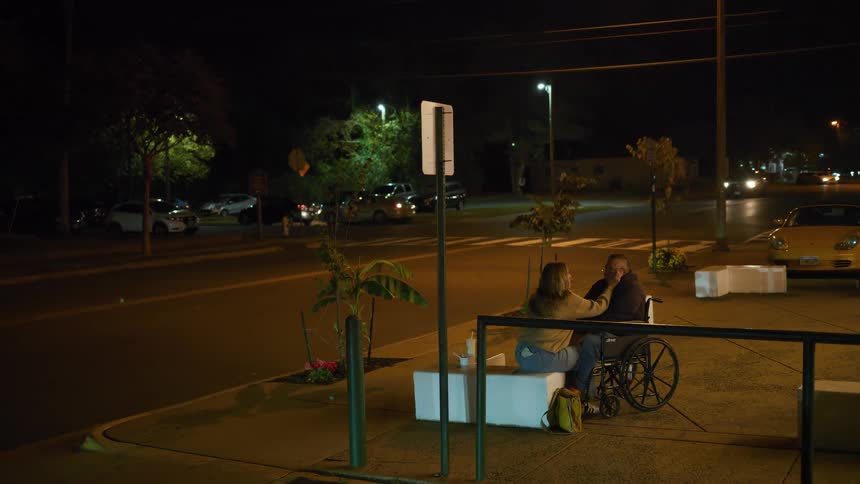 Couple sitting in an outdoor area at night while the man remains in a wheelchair