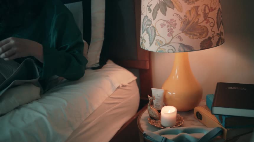 Woman sitting on the bed lights a candle with a lighter in her hand