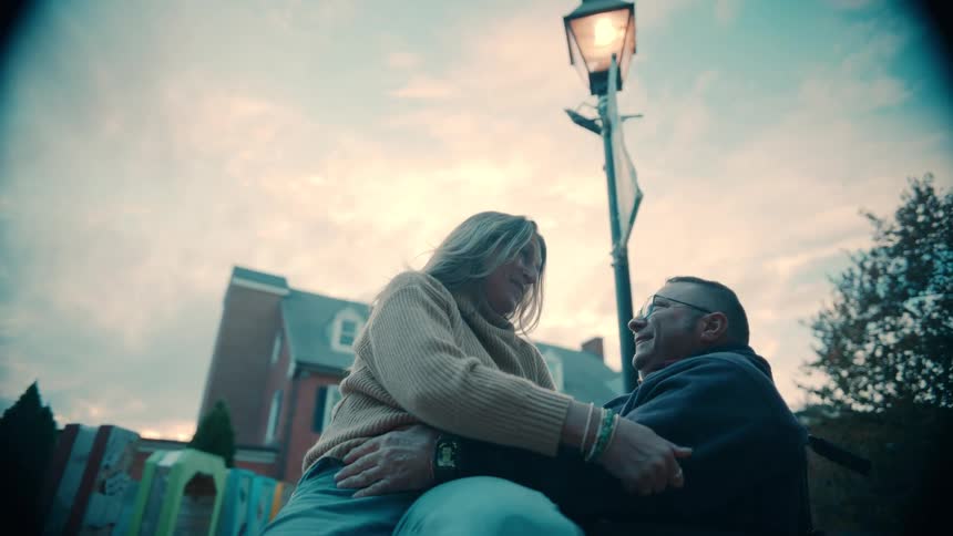 A middleaged couple sits outdoors in a public park at midday the woman resting on the mans lap as they engage in conversation