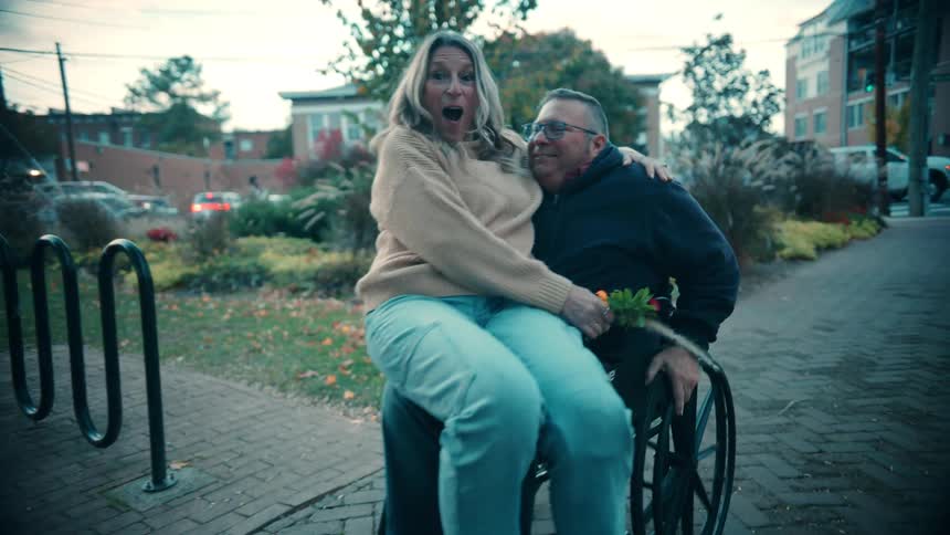 A woman sitting on a mans lap in a wheelchair