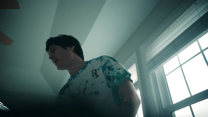 A young man is smiling as he tosses several pieces of clothing in front of him forming a pile