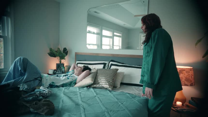 Man lies down on the bed while another woman lies beside him
