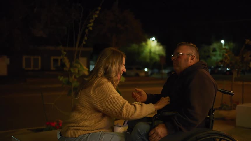 The woman helps a man in a wheelchair by feeding him