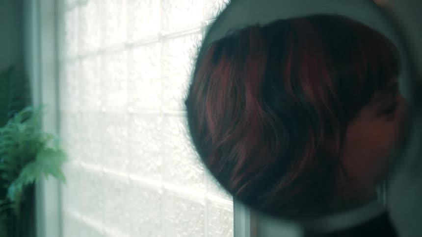 A young couple is inside the bathroom with the woman applying makeup to her face while looking at the mirror