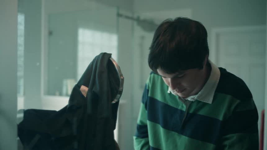 A teenage boy combs his hair in front of a bathroom mirror at midday