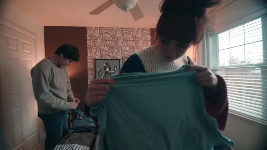 A woman holding a blue blouse in a room and then throwing it behind her