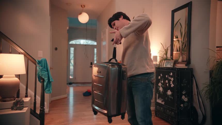 A male teenager weighing a travelling bag in a corridor indoors