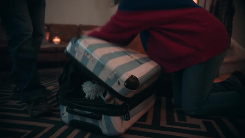 A woman is closing a suitcase that is full of clothes