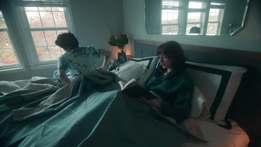 The woman reads in bed as the man wakes up