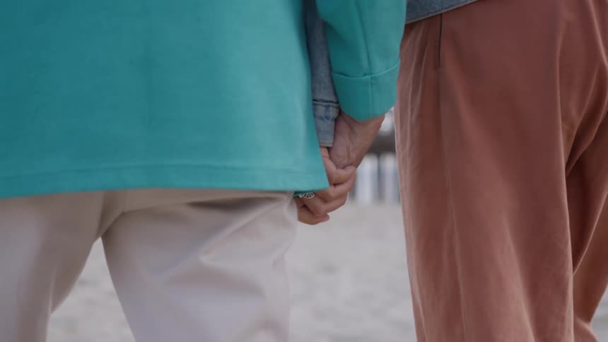 A couple walks hand in hand across the beach sand at midday