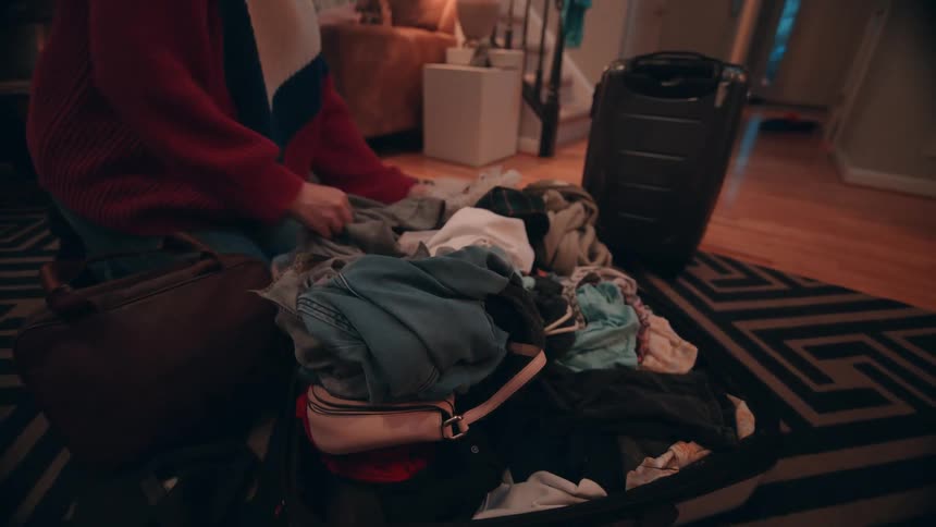 A woman is stuffing clothes in a travel case preparing for travel