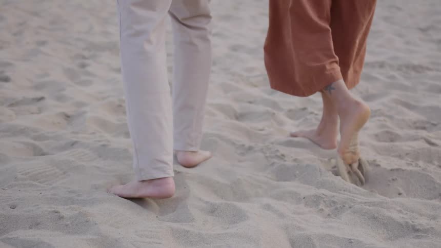 Bare feet walk through the sand lifting small trails of grains