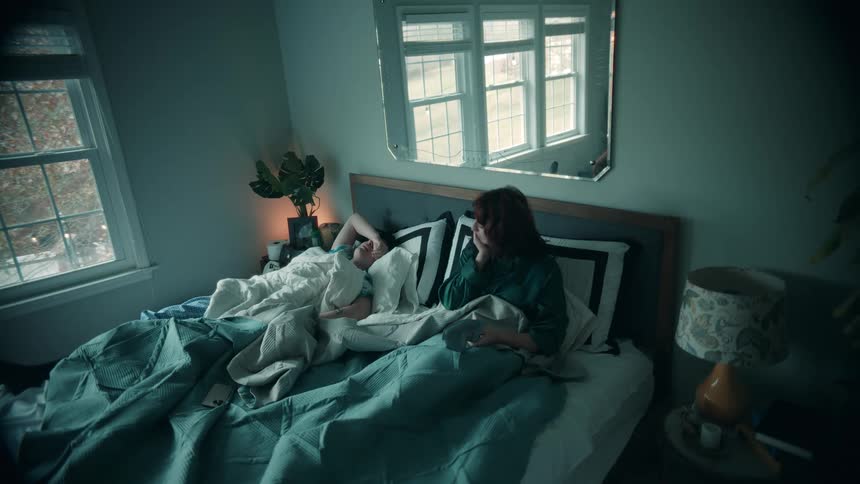 At daybreak a couple lies asleep in bed the woman wakes removes her blindfold turns to her side and switches on the reading lamp while her husband remains fast asleep beside her